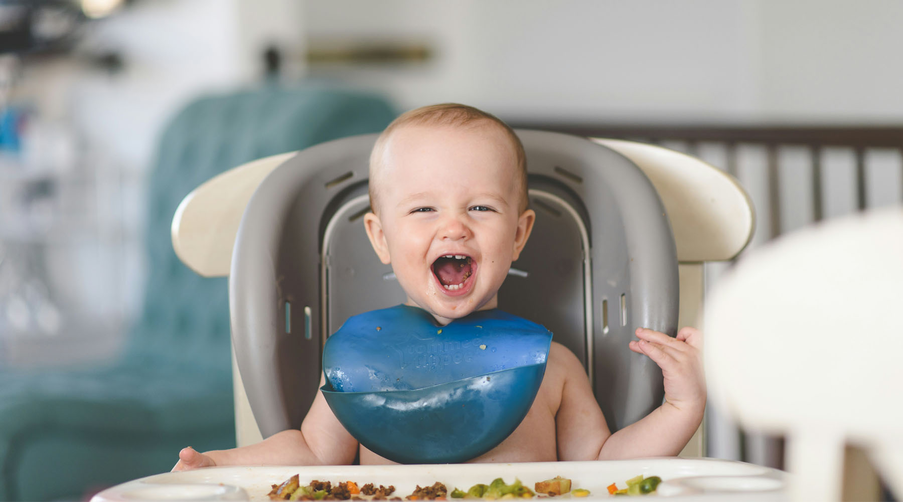 baby in a high chair eating vegetables