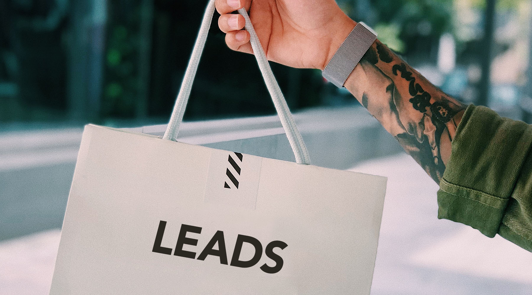 person with a heavily tattooed arm holding up a white bad with the word "leads" on it