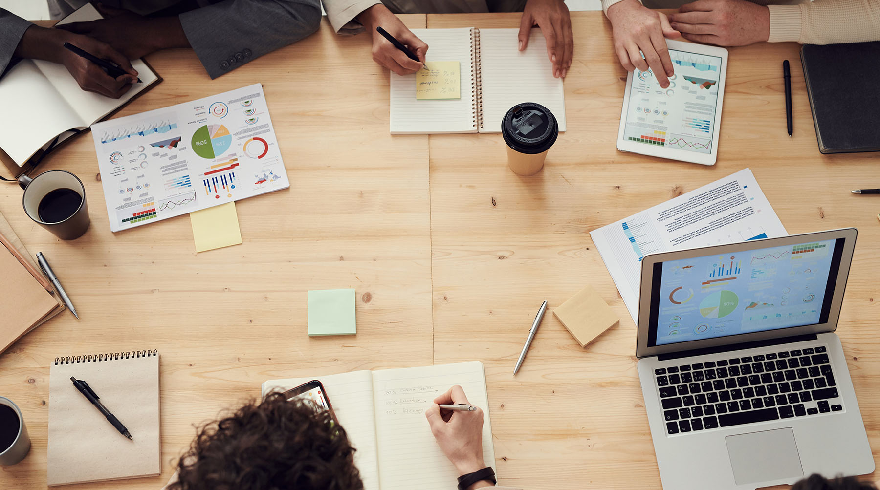 an aerial view of people surrounding a desk writing in notebooks and looking at charts